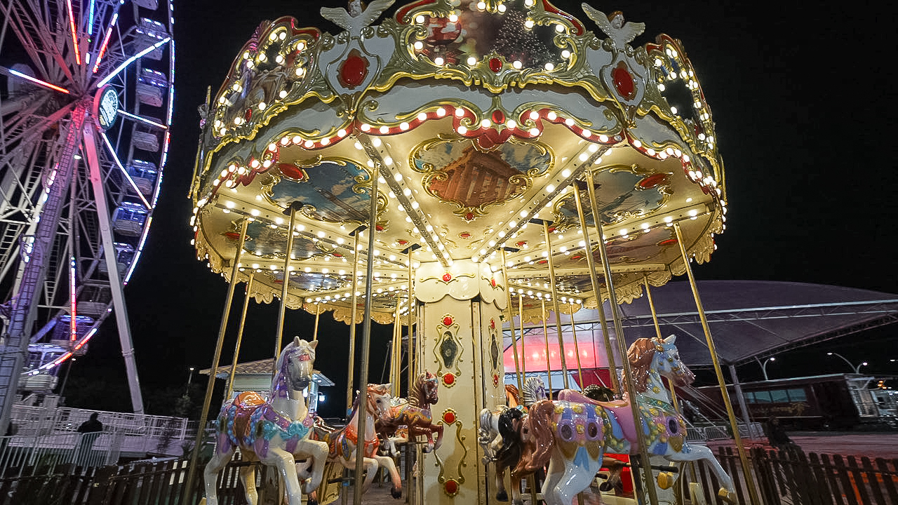 Carrossel iluminado com cavalos decorativos e roda gigante ao fundo